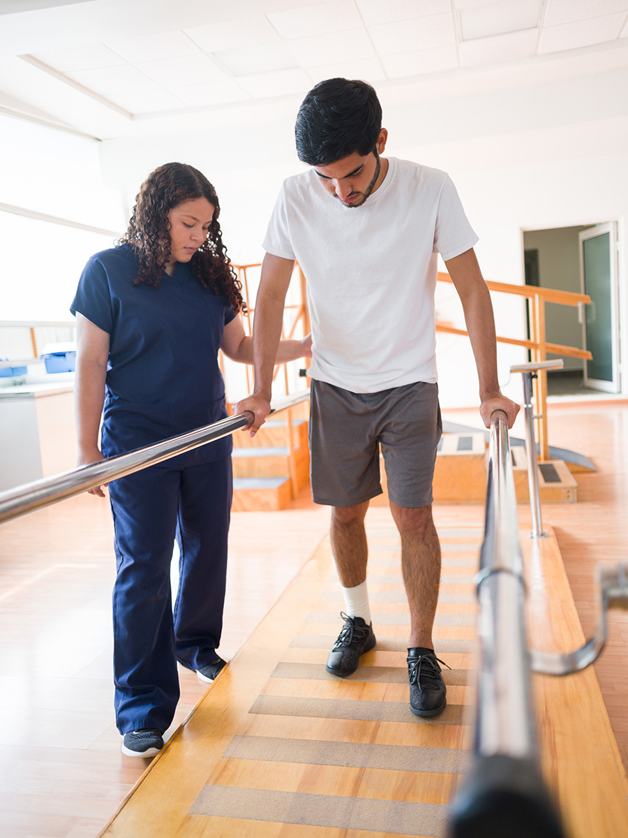 Athletic male walking in parallel bars with support